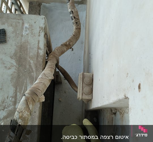 צינור עטוף בבד ליד קיר עם כתמי טיח